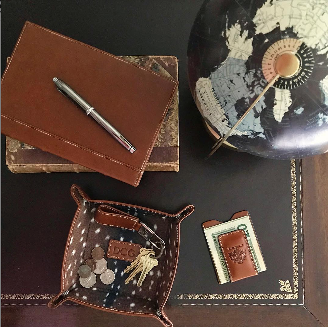 A British tan leather money clip with a pen, shown next to a valet tray and globe on a desk to illustrate its practical size, elegant design, and how it holds cards and cash efficiently, unlike bulky money clip wallets.
